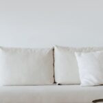 A chic minimalist living room featuring a white sofa with cushions, dried flowers in a vase, and a wooden floor.